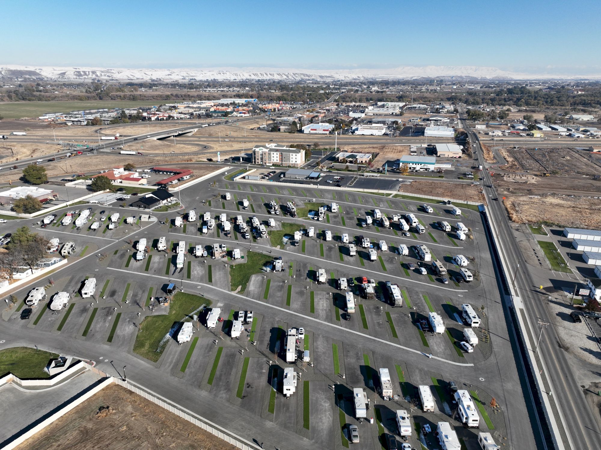 Aerial view of a large RV park with rows of trailers and campers, surrounded by roads and open fields, under a clear sky.