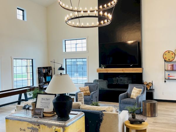 A cozy, modern living room with a black fireplace, circular chandelier, cream sofas, wooden accents, and large windows letting in natural light.
