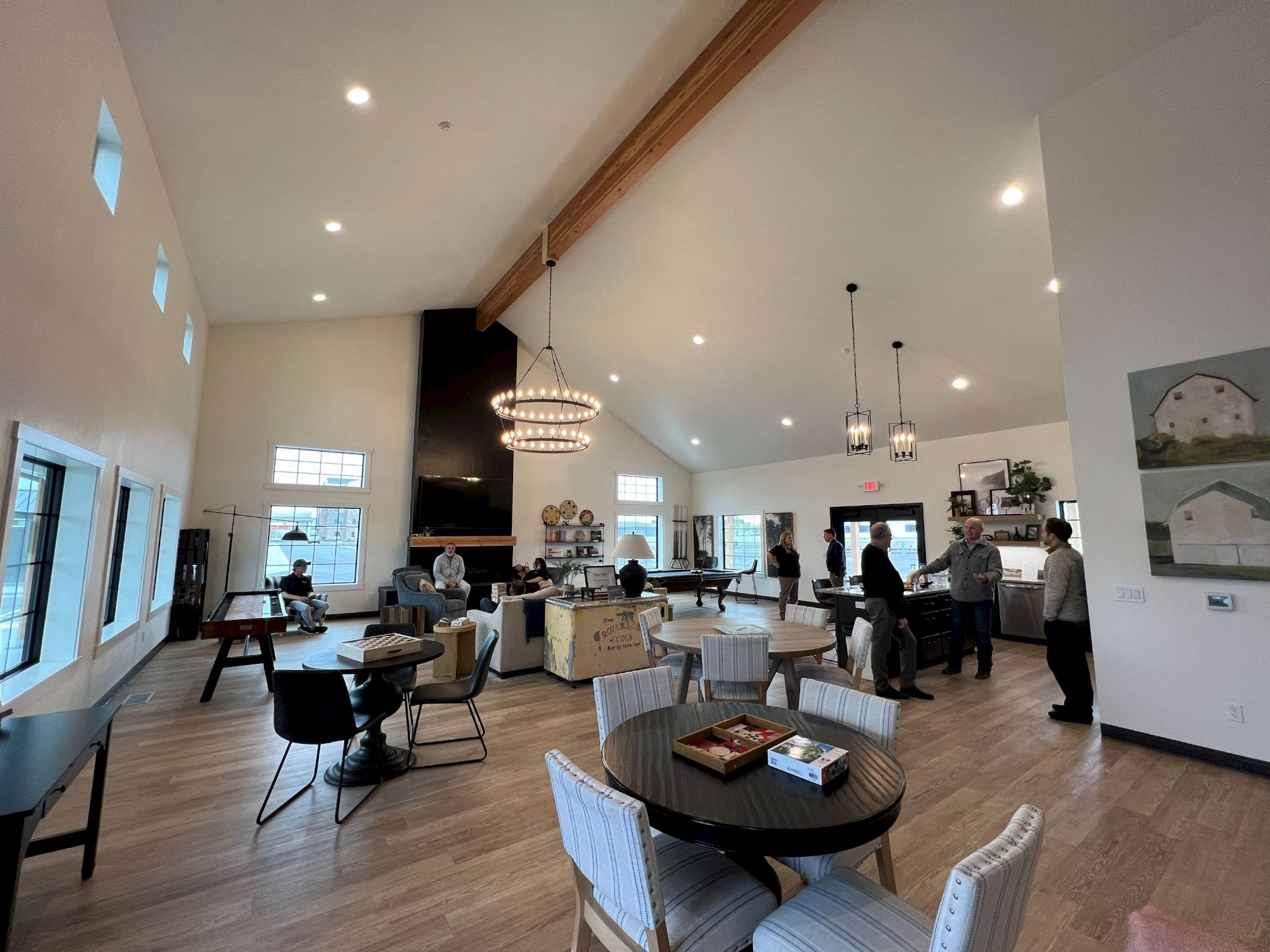 A bright, airy cafe with wooden floors, white walls, modern light fixtures, and several tables; people chat and order near the back.