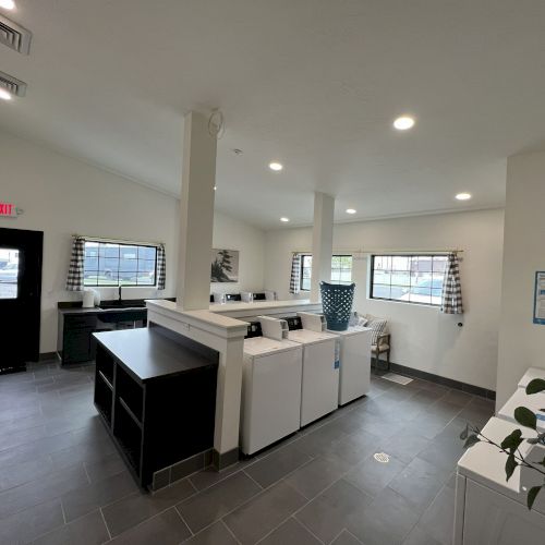 A bright office lobby or break room with white appliances, a central island, and large windows letting in light.
