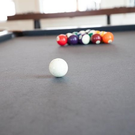 A white cue ball is in focus on a pool table, with a rack of colorful balls clustered in the background.
